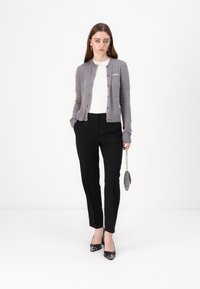 Grå cardigan med knapper, hvid top og skræddersyede sorte bukser. Sorte patenthæle og en lille metallic taske fuldender outfittet.
