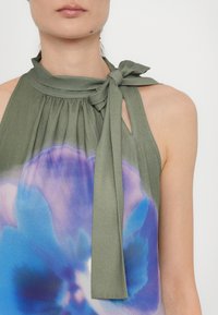 Groene mouwloze top met een striknek, uitgerust met een blauw en paars bloemgradientpatroon en geplisseerde details op de buste.