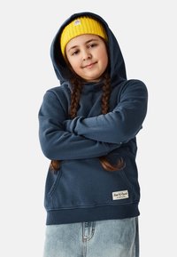 Merensininen huppari pehmeästä kankaasta, joissa on kengurun tasku ja resorit hihansuissa, yhdistetty kirkkaan keltaiseen neulottuun pipoon.