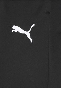 Schwarze Sporthose mit einem weißen Puma-Logo. Der Stoff ist glatt mit einer weichen Textur und Seitennahtdetails.