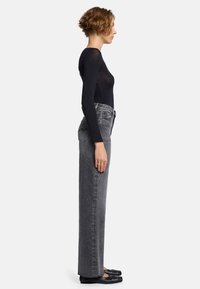 Jean gris taille haute avec une coupe droite et une texture délavée, associé à un haut noir ajusté à manches longues. Les chaussures sont des ballerines noires.