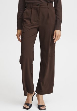 Braune weite Hosen mit Falten, seitlichen Taschen und einer glatten Textur. Kombiniert mit schwarzen offenen Absatzmules.