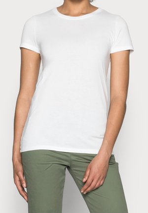 Persoon draagt een effen wit T-shirt met korte mouwen en olijfgroene broek, staand met ontspannen handen langs het lichaam.