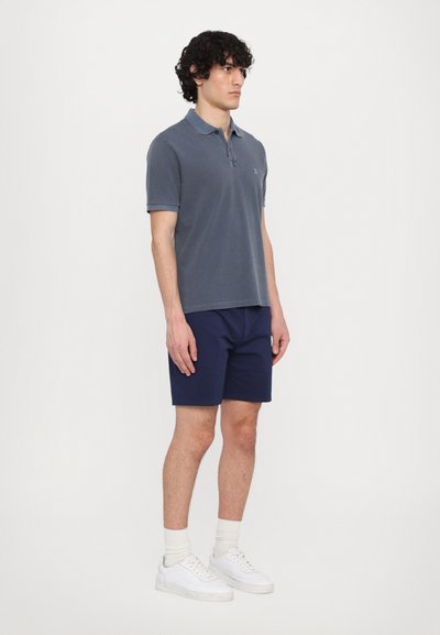Polo grigio con colletto, materiale in cotone, vestibilità slim; abbinato a pantaloni corti blu navy, sneakers bianche e calzini leggeri; design pulito.