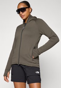 Olijfgroene zip-up hoodie met zijzakken, slim-fit ontwerp en duimgaten, gecombineerd met zwarte cargoshorts met een logo.