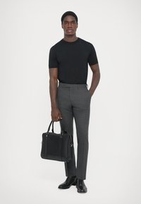 Camiseta negra de manga corta, pantalones grises a medida, zapatos de cuero negros y bolsa de cuero negro. Colores sólidos; texturas suaves; diseño moderno.