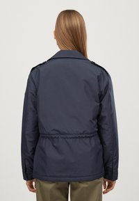 Mörkblå, lätt jacka med åtsittande midja, bred krage och axelklaffar. Har ett slätt, vattentåligt material.