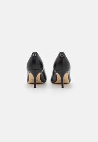 Zwarte leren hoge hakken met spitse neuzen, slanke hakken en reliëflogo-accenten op de achterkant. Gladde textuur, elegant ontwerp.