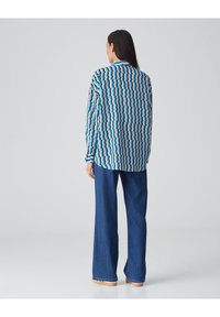 Koszula z długim rękawem w niebiesko-beżowo-białym wzorze zygzaka, zestawiona z szerokimi spodniami dżinsowymi w niebieskim kolorze. Posiada luźny krój i klasyczny kołnierzyk.