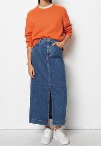 Maglione arancione a coste abbinato a una gonna di jeans blu a vita alta e lunghezza al ginocchio, con uno spacco frontale e tasche laterali, indossato con sneakers bianche.