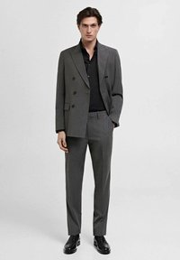 Double-breasted dark gray suit with a textured finish, paired with a black shirt and black shoes, featuring straight-cut trousers.
