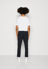 T-shirt blanche cropped et pantalon marine. Le pantalon possède une poche arrière, associé à des baskets blanches et des chaussettes mi-mollet. Design simple et minimal.