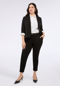 Czarna marynarka z podwiniętymi rękawami, biała koszula zapinana na guziki oraz dopasowane czarne spodnie. Spiczaste czarne szpilki. Gładka faktura materiału, dopasowany krój.