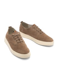 Braune Wildleder-Sneaker mit weißen Gummisohlen, runder Zehenpartie, Schnürdesign und minimalen Nähten. Mit einem Etikett, das einen kleinen Farbakzent aufweist.