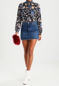 Blouse noire à fleurs avec des manches longues, mini-jupe en jean avec un ourlet effiloché, bottes blanches jusqu'à la cheville et un accessoire de pochette en fourrure rouge.