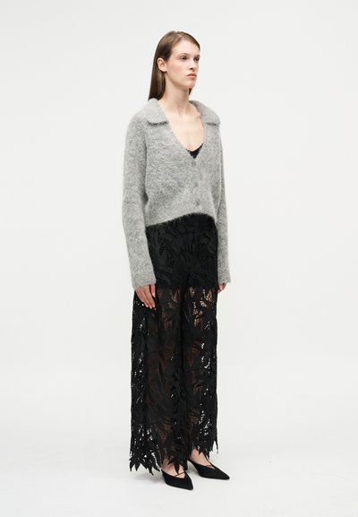 Γκρι κοντή ζακέτα από απαλό, χνουδωτό υλικό με γιακά και κούμπωμα με κουμπιά, συνδυασμένη με μαύρη, διάφανη, μάξι φούστα με φύλλωμα.