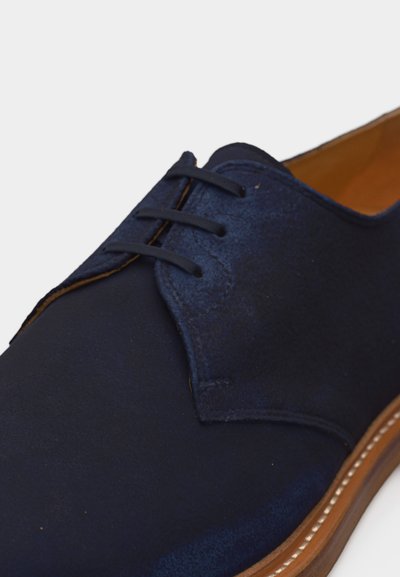 Ανδρικό δετό παπούτσι από σουέντ σε ναυτικό μπλε χρώμα με καφέ δερμάτινη σόλα και επένδυση σε ταμπά χρώμα, εμφανιζόμενο σε κοντινή γωνία.