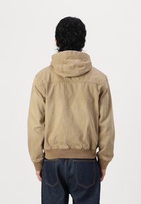 Hooded beige sweatshirt with a relaxed fit, featuring ribbed cuffs and hem, made from soft fabric with a textured finish.