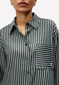 Green and white striped shirt made of smooth fabric, featuring a chest pocket, button closure, and classic collar design.