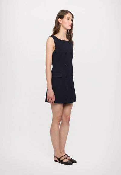 Rochie fără mâneci de culoare navy cu o siluetă ajustată, design dublu butonat, cinci butoane și două buzunare frontale. Purtați cu balerini negri.