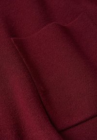 Burgunderstoff, weiche Textur, hat eine glatte Oberfläche mit subtiler glänzender Optik, zeigt einen gefalteten Rand und ein genähtes Taschendetail.