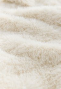 Tissu en fausse fourrure couleur crème avec une texture douce et pelucheuse et des fibres longues, disposé en plis ondulés. Idéal pour les couvertures ou le rembourrage.