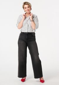 Zwarte wijde jeans gecombineerd met een wit gestreept shirt. Het shirt heeft een v-hals en opgerolde mouwen, terwijl levendige rode hakken de outfit compleet maken.