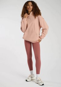 Rosa hoodie med framficka, avslappnad passform. Ett par rosafärgade leggings, vita sportstrumpor och ljusa sneakers med detaljer.