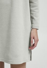 Helles graues Sweaterkleid, gerippte Textur, lange Ärmel, seitliche Schlitze, lässiger Schnitt, weicher Stoff, reicht bis zur Mitte des Oberschenkels, lässiges Design.