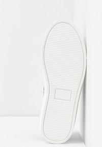 Bílá podrážka tenisky s texturovaným povrchem, zaobleným tvarem, černým lemem a razítkovanými detaily včetně velikosti a "Vyrobeno ve Španělsku".