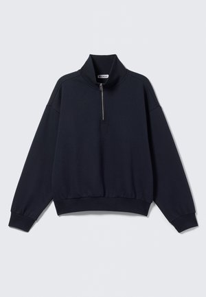 Sudadera de punto azul marino con un cuello alto y media cremallera. Presenta puños y dobladillo acanalados, tejido suave y un corte relajado.