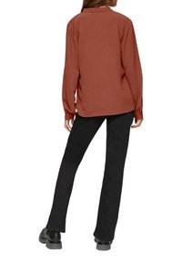 Bluzka z długim rękawem w kolorze rdzy z teksturowanej tkaniny, noszona na czarnych spódnicach w kształcie litery A i masywnych czarnych butach, widziana z tyłu.