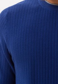 Blå ribbad stickad tröja med en texturerad yta och en rund halsringning. Tyget verkar mjukt och något elastiskt.