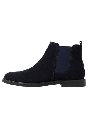 Bota corta de ante azul marino oscuro con paneles laterales elásticos, una lengüeta para tirar y una suela de goma texturizada. Diseño simple y elegante.