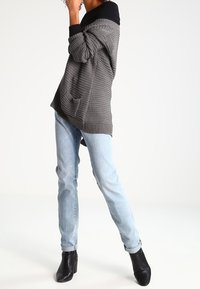 Gray knitted sweater with a black collar, paired with light blue jeans and black ankle boots. Sweater features a front pocket and ribbed texture.