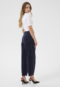 Top bianco attillato a maniche corte abbinato a pantaloni larghi blu scuro, con una delicata texture e una tasca sul retro. Scarpe col tacco nere a strap.