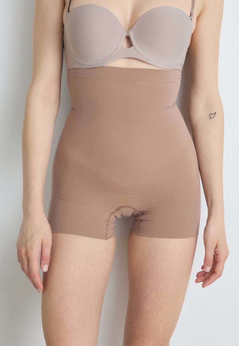 Beige seamless shapewear shorts with high waist, elastic material, and a small gusset opening, designed for comfort and a smooth silhouette.