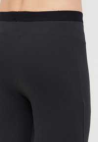 Leggings noirs extensibles avec une texture lisse et une taille élastique. Le tissu semble respirant et moulant. Pas de motifs visibles.
