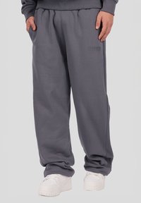 Grå træningsbukser med elastisk taljebånd, sidelommer og præget logodetalje på låret. Fremstillet af blødt, tekstureret stof.