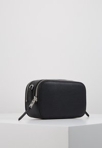 Borsa rettangolare in pelle nera con superficie testurizzata, zip argentata e manico breve. Presenta un design minimalista e una forma compatta.