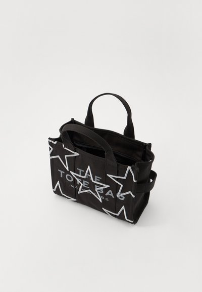 Svart tote bag med hvitt stjernemønster og logo-tekst. Den har to håndtak, har glidelås og er laget av slitesterk stoff.
