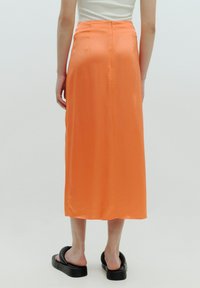 Lange, orange-satinierte Rock mit einem Reißverschlussdetail hinten, glatt in der Textur und gerader Schnitt, der bis zur Mitte der Wade reicht.