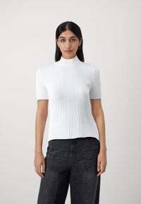 Witte geribbelde top met korte mouwen en hoge hals. Heeft een aansluitend ontwerp en een gladde textuur, gecombineerd met donkerdenim high-waisted broek.