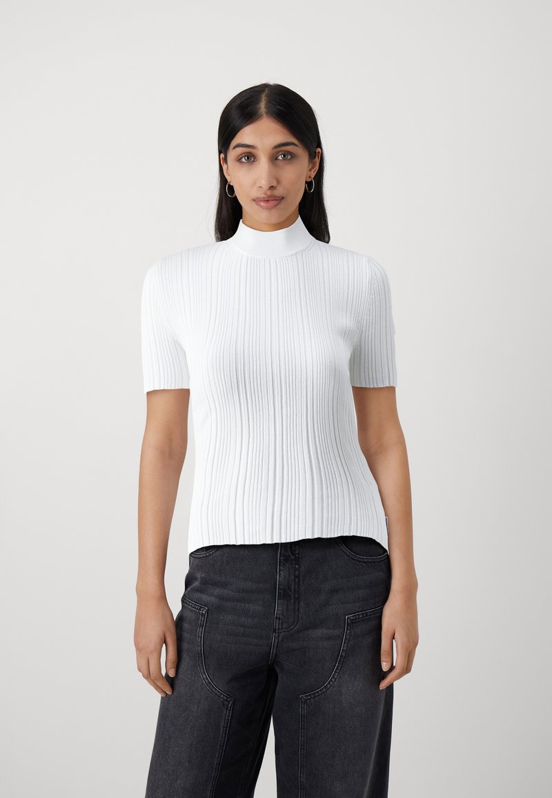 Witte geribbelde top met korte mouwen en hoge hals. Heeft een aansluitend ontwerp en een gladde textuur, gecombineerd met donkerdenim high-waisted broek.