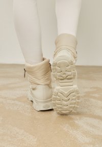 Bottes blanches épaisses avec un col rembourré, des semelles en caoutchouc texturé et des fermetures éclair sur les côtés. Le matériau semble lisse et légèrement brillant.