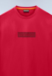 Κόκκινο βαμβακερό t-shirt με ανάγλυφο μαύρο κουτί λογότυπου με το κείμενο "NAPAPIJRI", στρογγυλή λαιμόκοψη με πορτοκαλί εσωτερική ταινία, κοντά μανίκια.