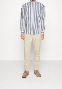 Gestreiftes Langarmhemd in Grau und Weiß mit einem knöpfbaren Kragen, kombiniert mit beigen Hosen und taupefarbenen Wildlederschuhen.