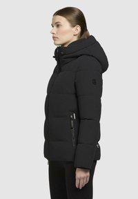 Doudoune noire avec capuche, design matelassé et deux poches latérales zippées. Le tissu semble lisse et isolé.