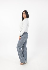 Ljusgrå, texturerad tröja i kombination med ljusblå, utsvängda jeans. Jeansen har synliga sömmar och fickor, vilket visar en avslappnad design.