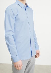Chemise à manches longues bleu clair, avec un col classique et des poignets standards, fabriquée en un mélange de coton lisse.